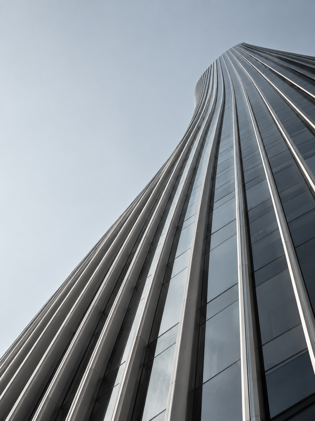 An upward view of sculptural glass and metal architecture against a clear sky